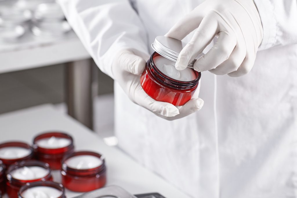 Lab worker in white gown and gloves holding skin care product